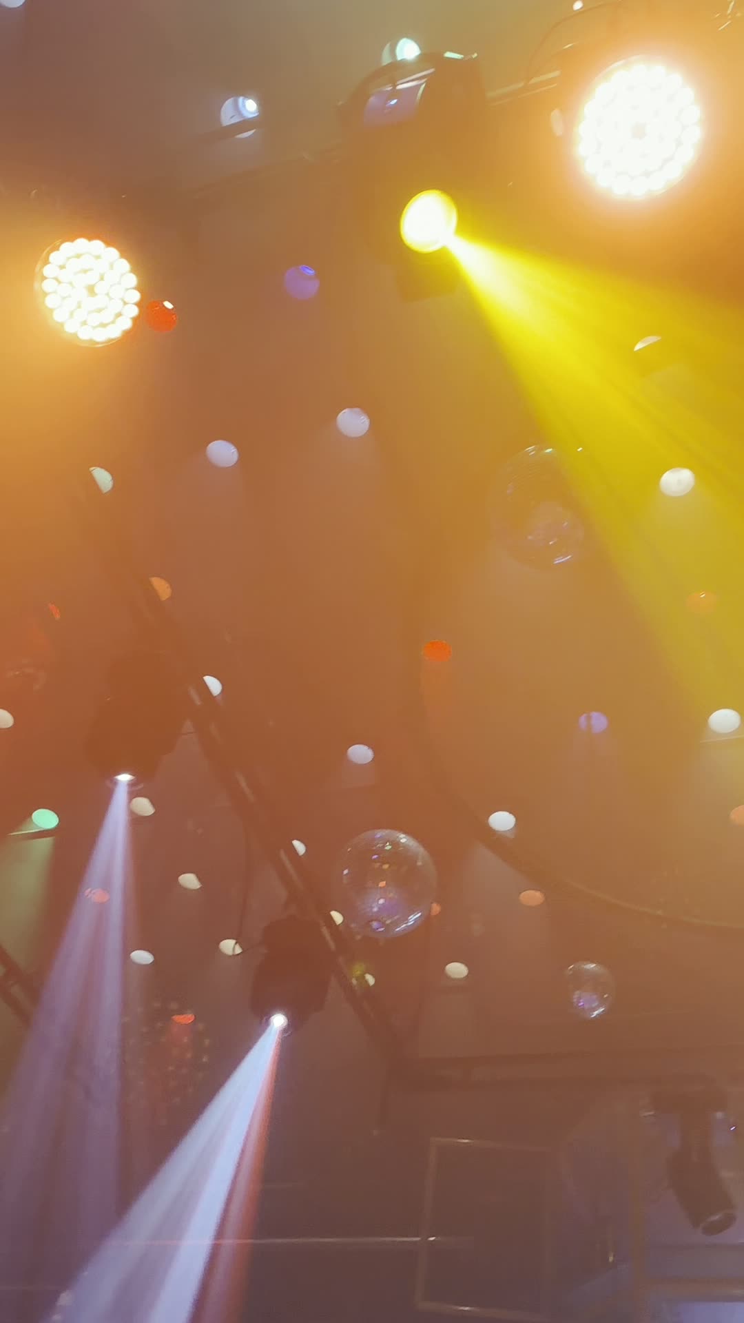 Amber and yellow stage lights and a mirror ball on the ceiling truss above the gym floor