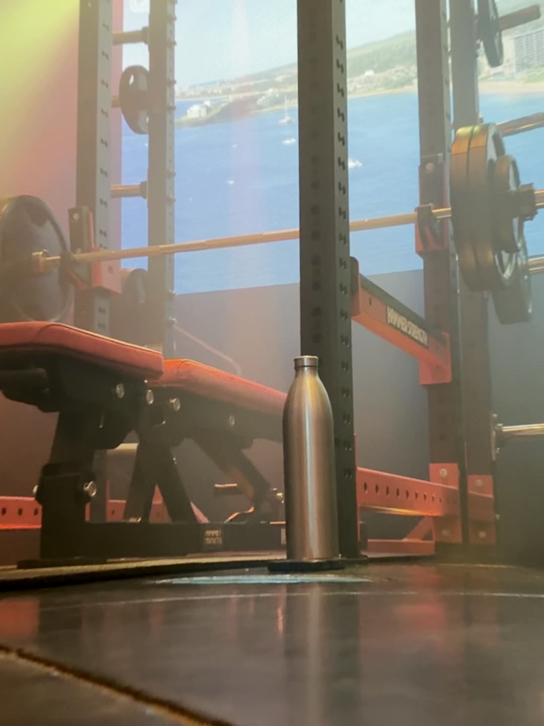 Bench and rack in front of an LED panel showing open water, with a water bottle on the floor